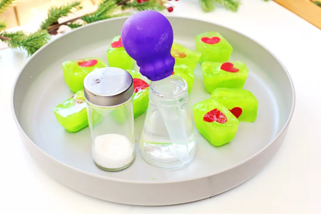 Grinch's Frozen Heart Activity - Cultivating Brilliant Minds melted green ice cubes with red hearts, a pipette, and salt