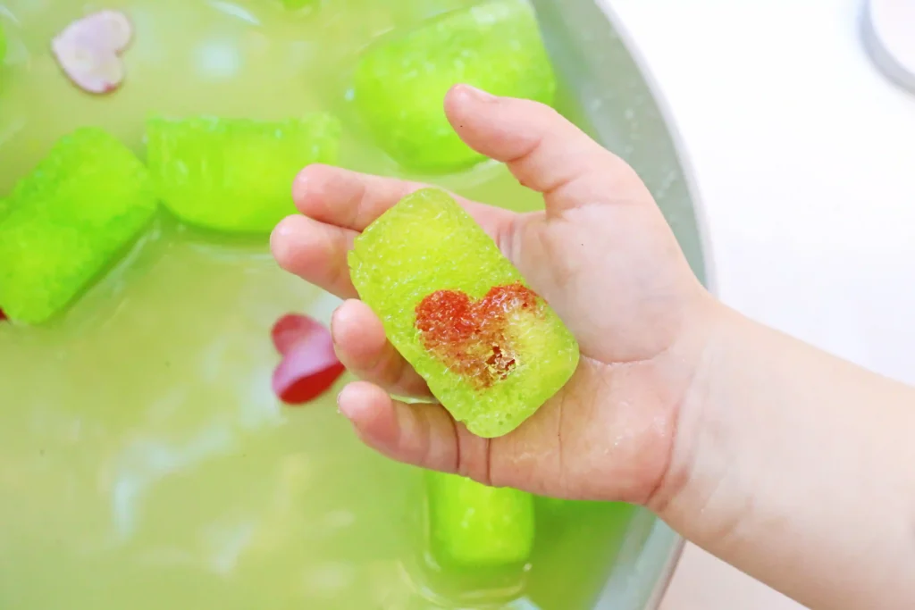 Grinch's Frozen Heart Activity - Cultivating Brilliant Minds a kid holding a green ice cube with a heart frozen inside