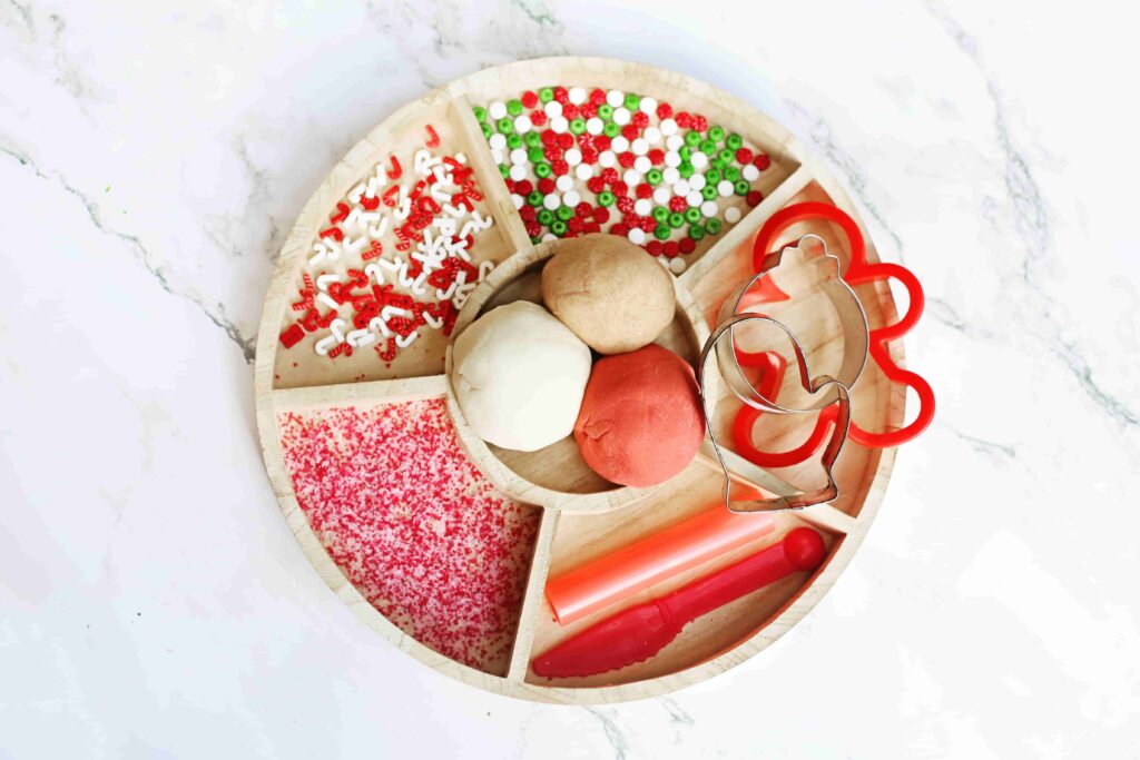 Holiday Cookie Playdough Bakery Tray - Cultivating Brilliant Minds a playdough tray filled with holiday-related items like red and green sprinkles and gingerbread cookie cutters