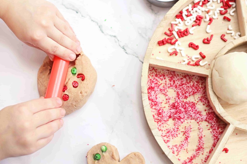 Holiday Cookie Playdough Bakery Tray - Cultivating Brilliant Minds a kid rolling out cinnamon playdough with sprinkles in in