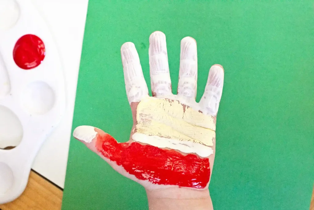 Handprint Santa Ornament - Cultivating Brilliant Minds a kid's hand painted with red, tan, and white paint