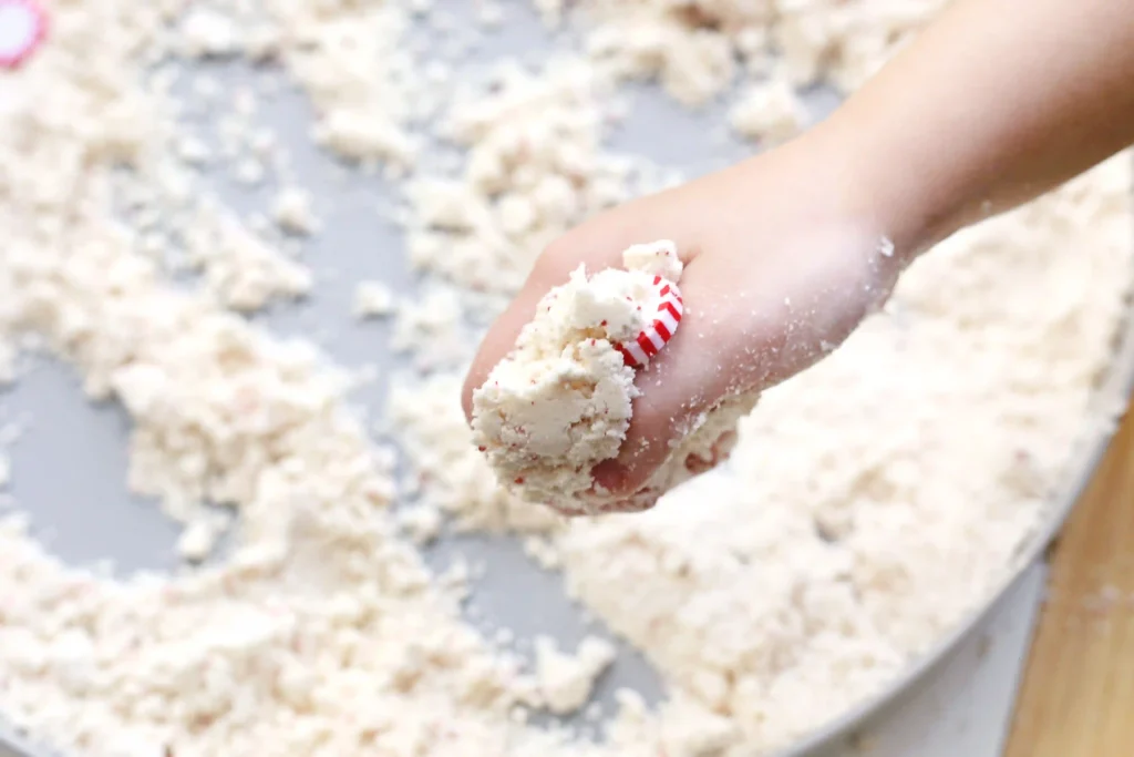 Peppermint Latte Cloud Dough Tray - Cultivating Brilliant Minds a kid holding the cloud dough with peppermints