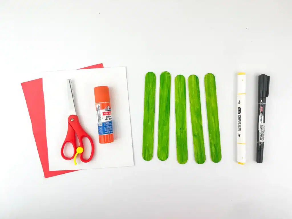 Grinch Popsicle Stick Craft - Cultivating Brilliant Minds popsicle sticks painted green, a marker, glue, scissors, and red and white construciton paper