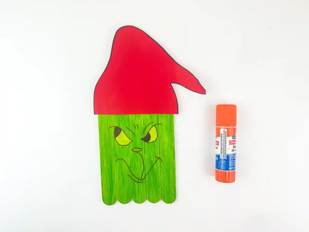 Grinch Popsicle Stick Craft - Cultivating Brilliant Minds popsicle sticks glued together and painted green with a grinch face and a red santa hat