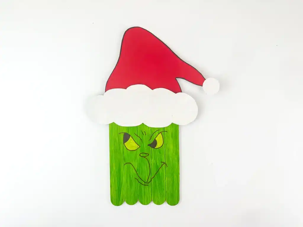 Grinch Popsicle Stick Craft - Cultivating Brilliant Minds popsicle sticks glued together and painted green with a grinch face and a red santa hat