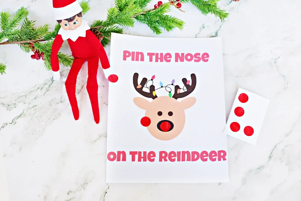 Pin the Nose on the Reindeer - Cultivating Brilliant Minds an elf on the shelf next to red dot stickers and a sign that reads "pin the nose on the reindeer"