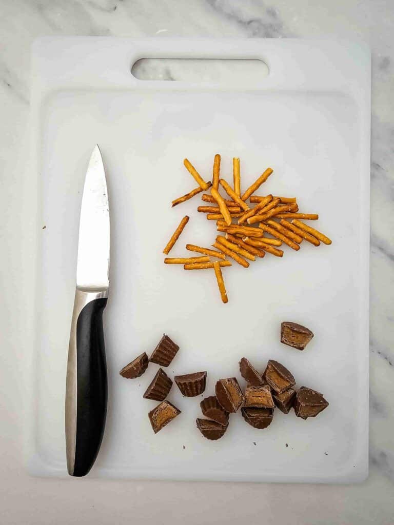 Melted Snowman Chocolate Bark - Cultivating Brilliant Minds resee's cut in half and pretzel rods on a tray