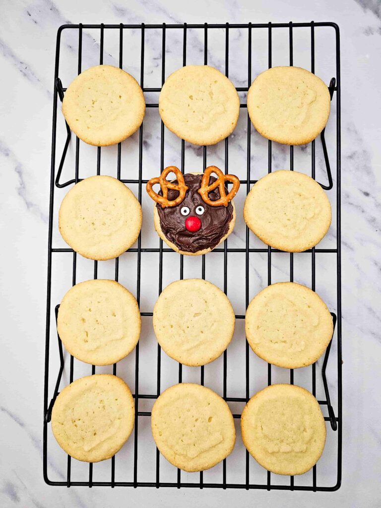 Reindeer Sugar Cookies - Cultivating Brilliant Minds cookies on a cooling rack. one cookie is decorated to look like a reindeer