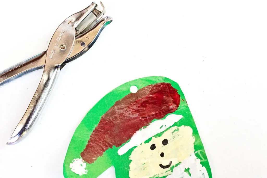 Handprint Santa Ornament - Cultivating Brilliant Minds a handprint made to look like santa on green construction paper with a hole punched at the top