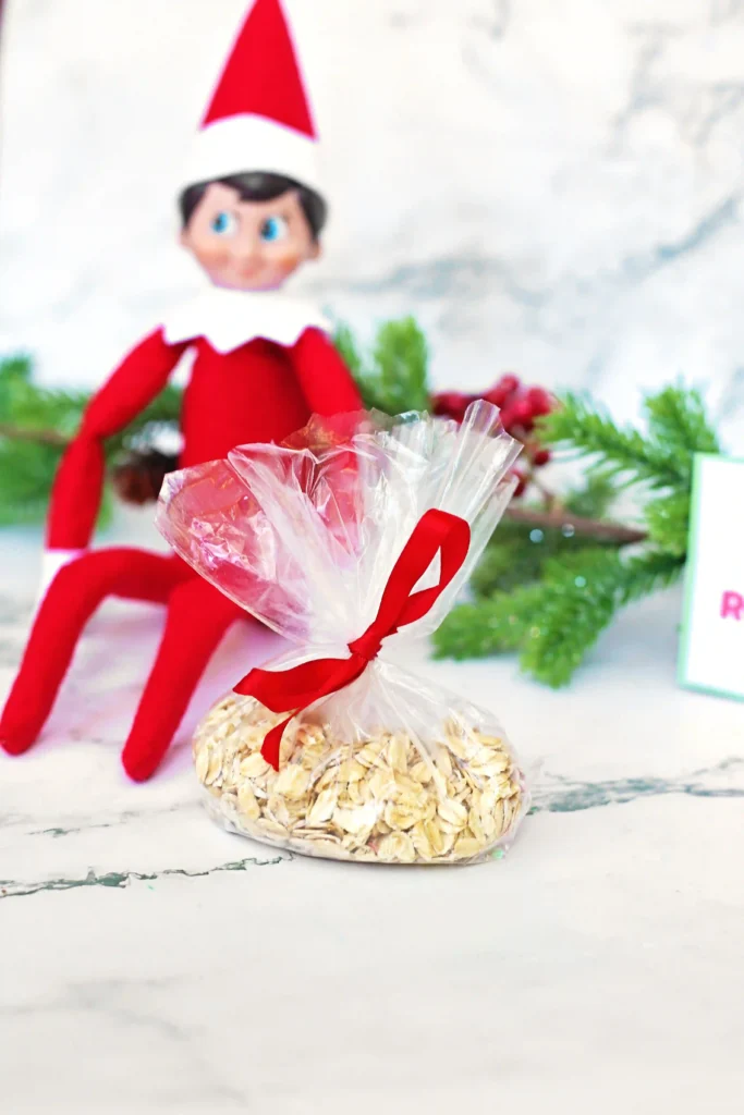 Elf on the Shelf Reindeer Food Craft - Cultivating Brilliant Minds elf on the shelf next to a bag of oats and glitter
