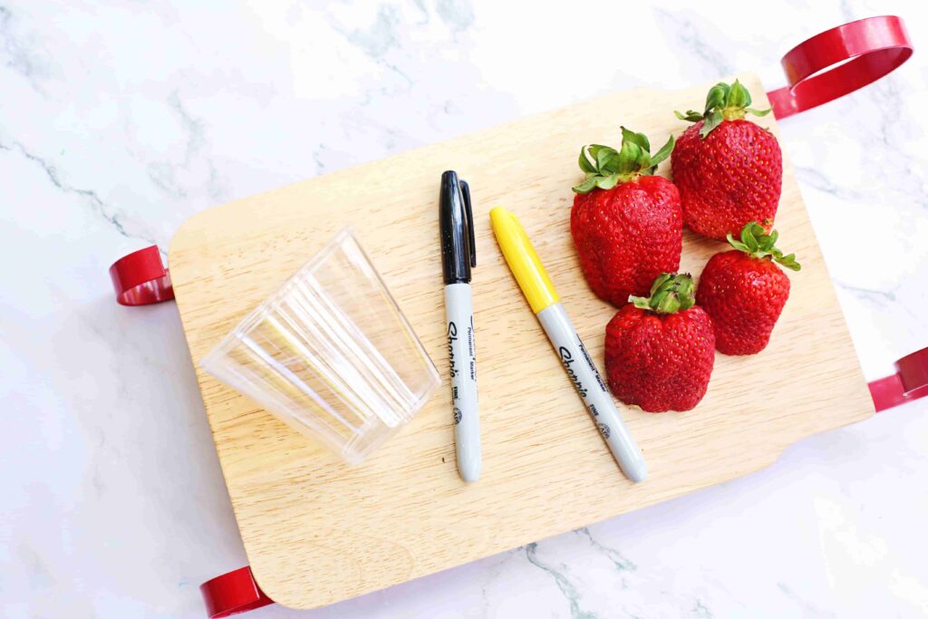 Santa Fruit Cups - Cultivating Brilliant Minds a clear plastic cup, black and yellow sharpies, and strawberries