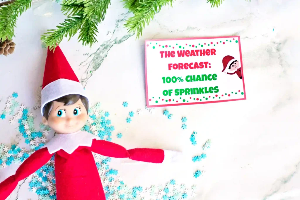 Elf on the Shelf Idea Snow Angel - Cultivating Brilliant Minds an elf on the shelf making a snow angel in sprinkles with a sign that reads "the weather forecast: 100% chance of sprinkles"