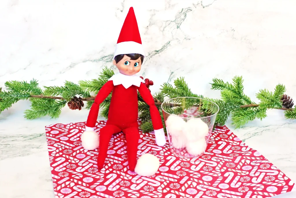 Elf on the Shelf Idea: Snowball Toss Game - Cultivating Brilliant Minds an elf on the shelf with a plastic cup and cotton balls