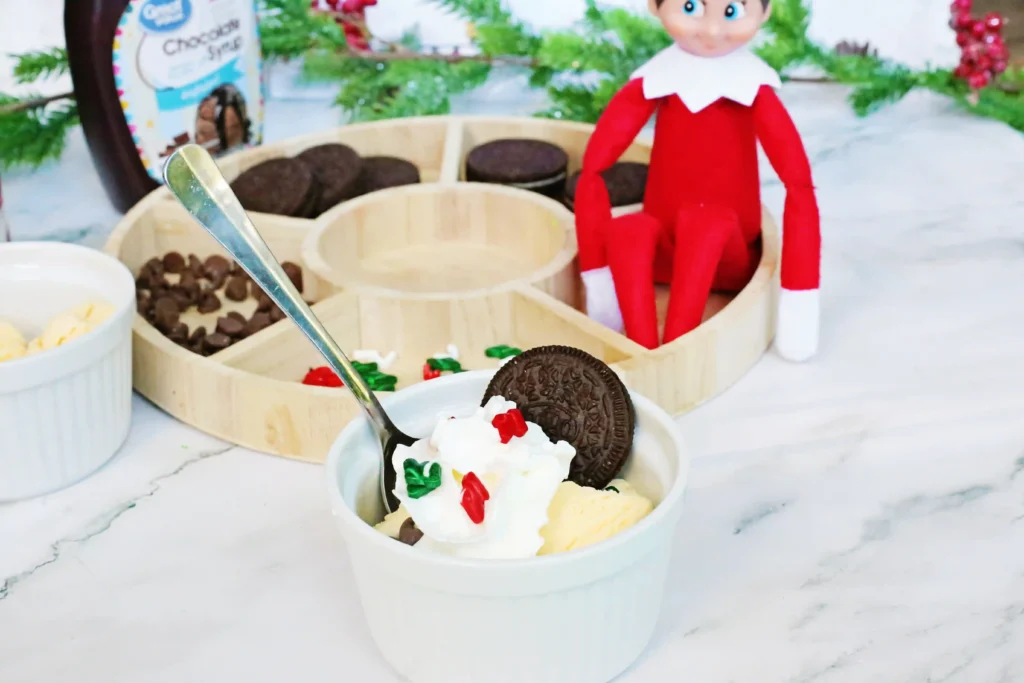 Elf on the Shelf Idea - Cultivating Brilliant Minds a bowl of ice cream with toppings and an elf on the shelf in the background