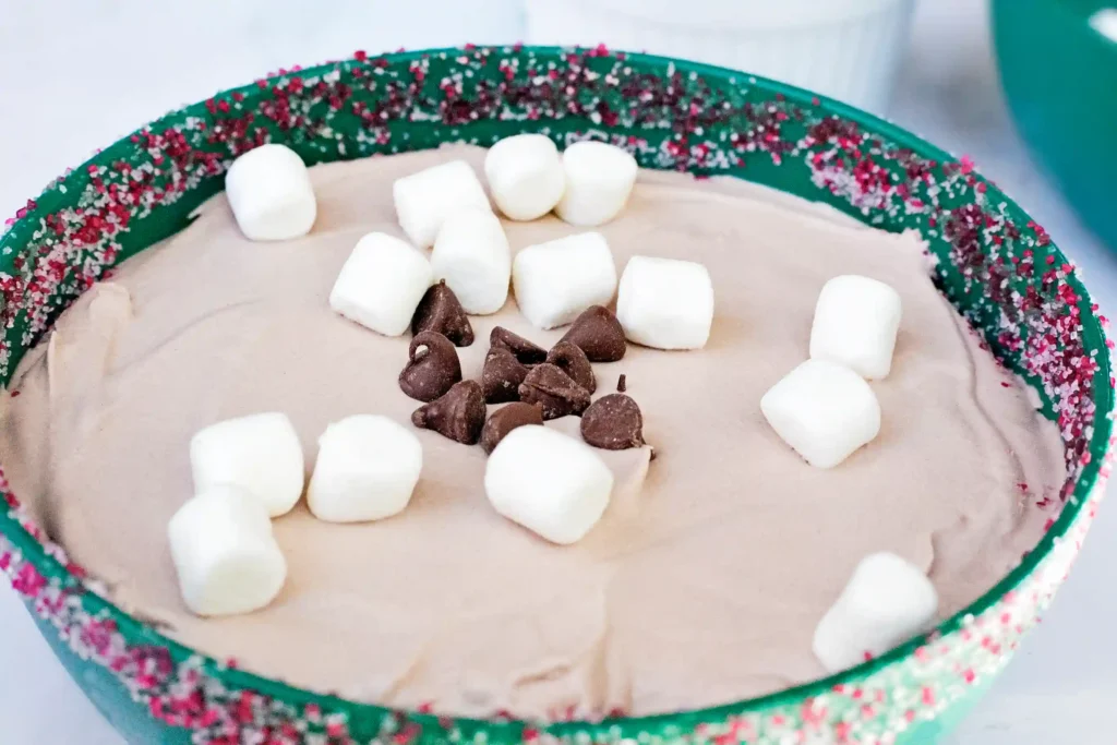 Hot Cocoa Dip - Cultivating Brilliant Minds hot cocoa dip with marshmallows and chocolate chips in a green bowl with sprinkles around the rim