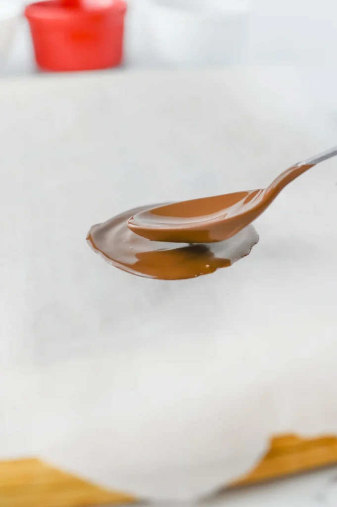 Reindeer Bark for Christmas - Cultivating Brilliant Minds putting melted chocolate on parchment paper with a spoon