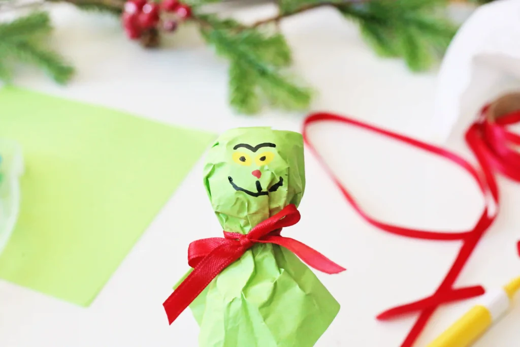 Grinch Lollipops - Cultivating Brilliant Minds a lollipop covered with green tissue paper and decorated to look like the grinch