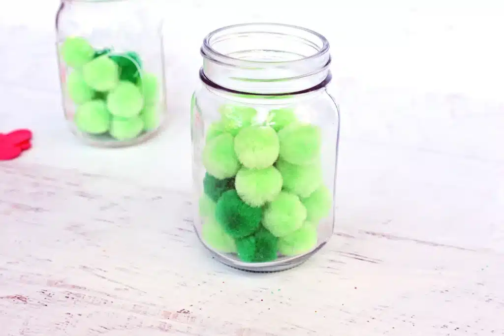 Grinch Heart Jar Challenge - Cultivating Brilliant Minds green pom poms in a mason jar