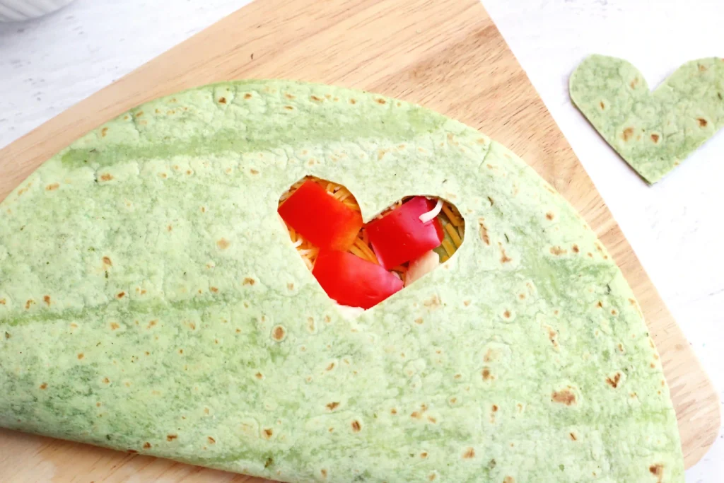 Grinch Quesadillas - Cultivating Brilliant Minds a quesadilla with a heart cut out and red peppers inside