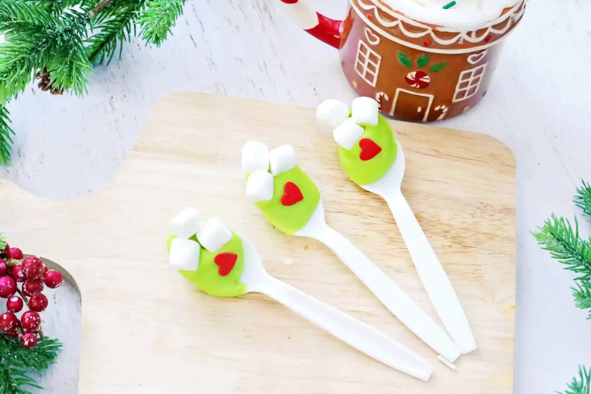 spoons with green-colored white hot chocolate melted on it with mini marshmallows and a red candy heart