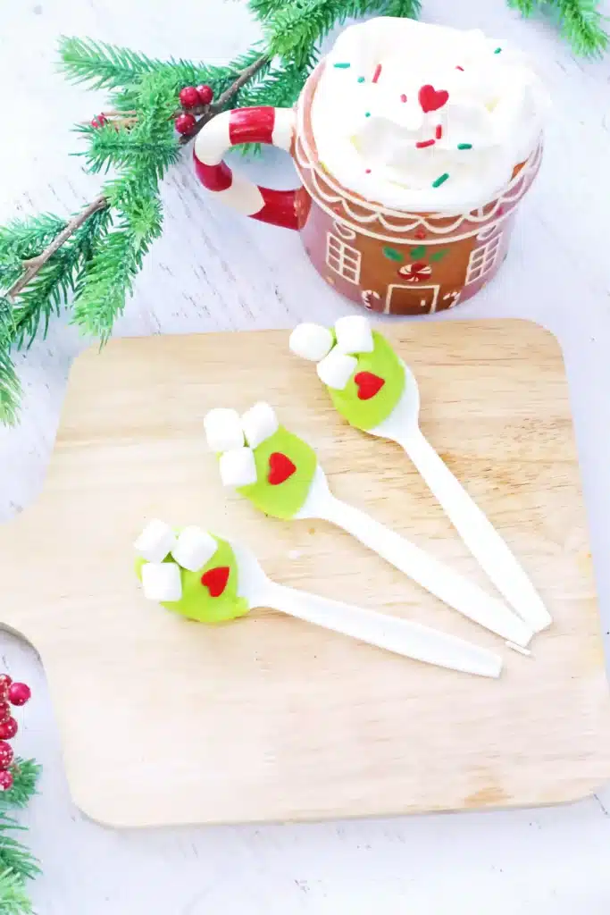 Grinch Hot Chocolate Spoons - Cultivating Brilliant Minds spoons with green-colored white hot chocolate melted on it with mini marshmallows and a red candy heart