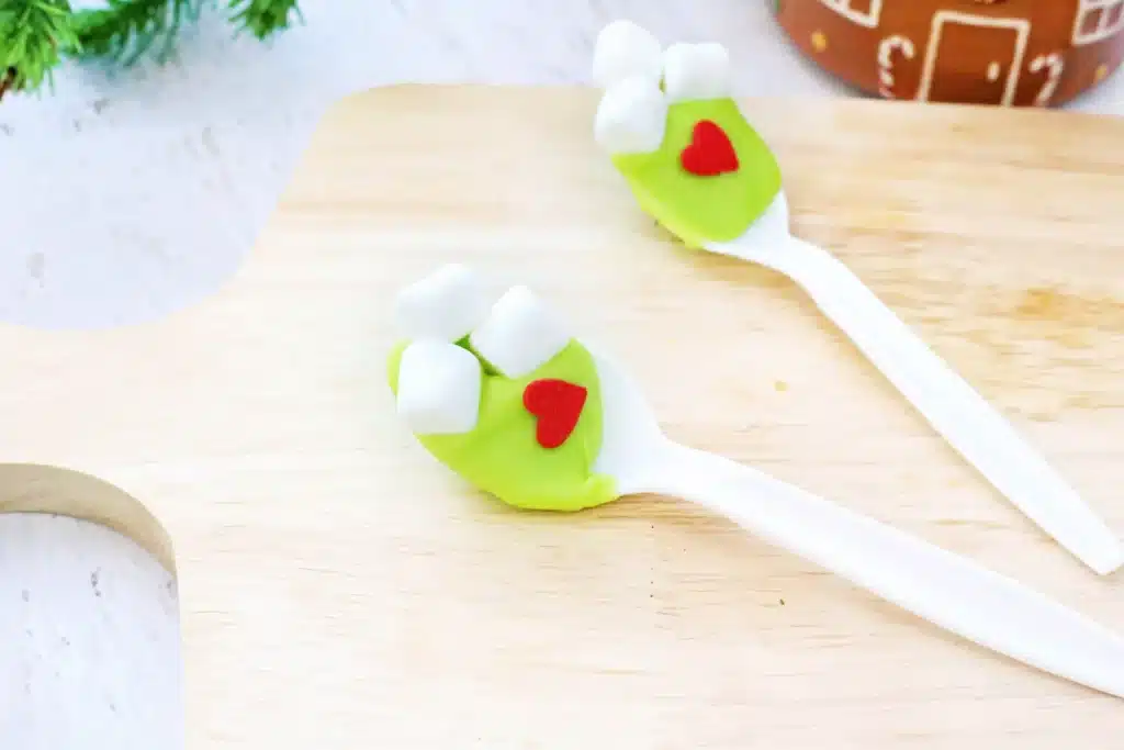 Grinch Hot Chocolate Spoons - Cultivating Brilliant Minds spoons with green-colored white hot chocolate melted on it with mini marshmallows and a red candy heart
