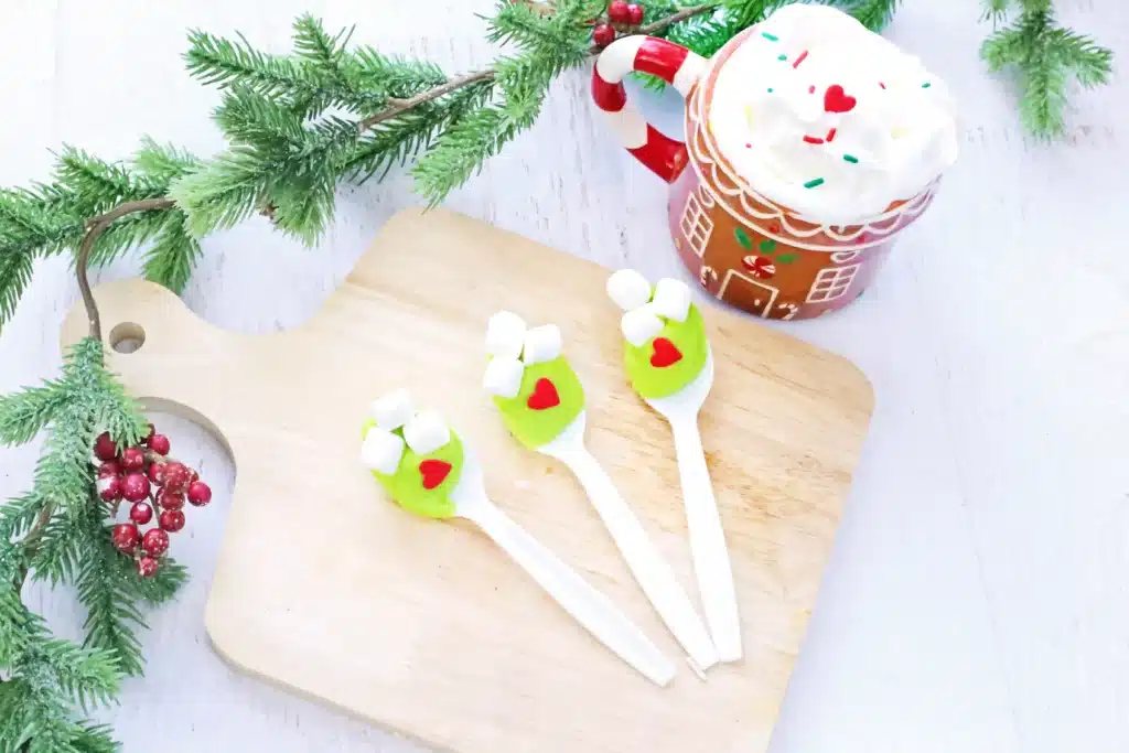 Grinch Hot Chocolate Spoons - Cultivating Brilliant Minds spoons with green-colored white hot chocolate melted on it with mini marshmallows and a red candy heart