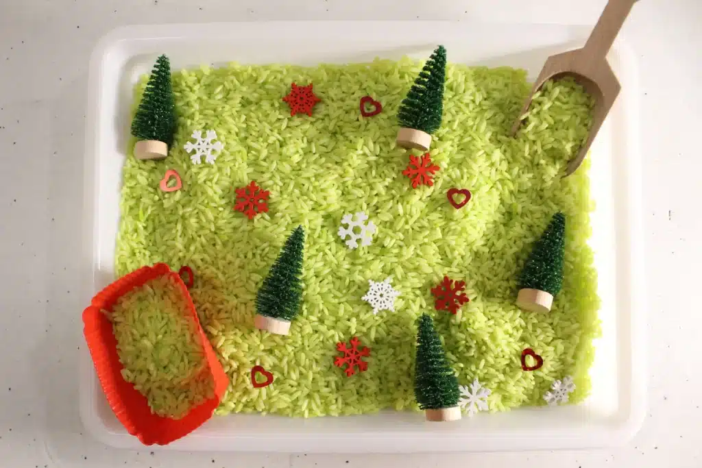 Grinch Sensory Bin - Cultivating Brilliant Minds a grinch sensory bin using green rice, christmas trees, and snowflakes
