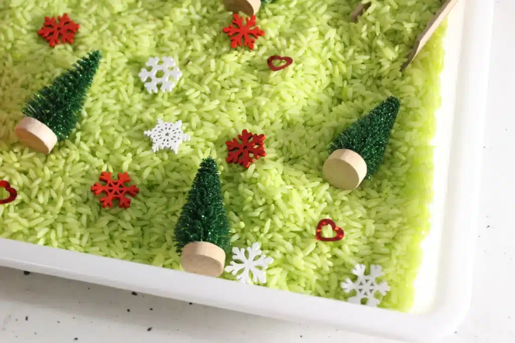 Grinch Sensory Bin - Cultivating Brilliant Minds a grinch sensory bin using green rice, christmas trees, and snowflakes