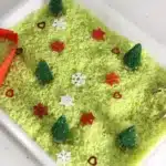 Grinch Sensory Bin - Cultivating Brilliant Minds a grinch sensory bin using green rice, christmas trees, and snowflakes
