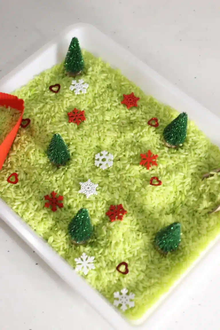 a grinch sensory bin using green rice, christmas trees, and snowflakes