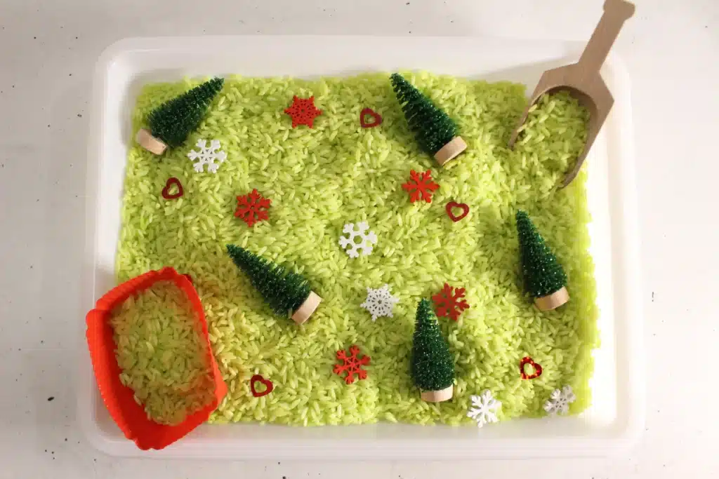 Grinch Sensory Bin - Cultivating Brilliant Minds a grinch sensory bin using green rice, christmas trees, and snowflakes