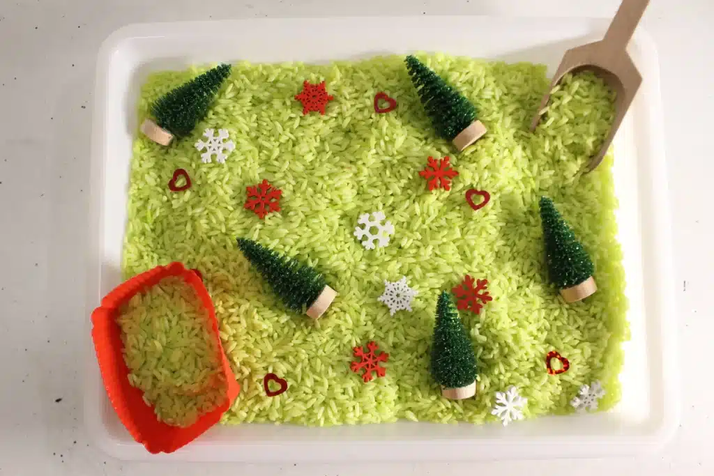 Grinch Sensory Bin - Cultivating Brilliant Minds a grinch sensory bin using green rice, christmas trees, and snowflakes