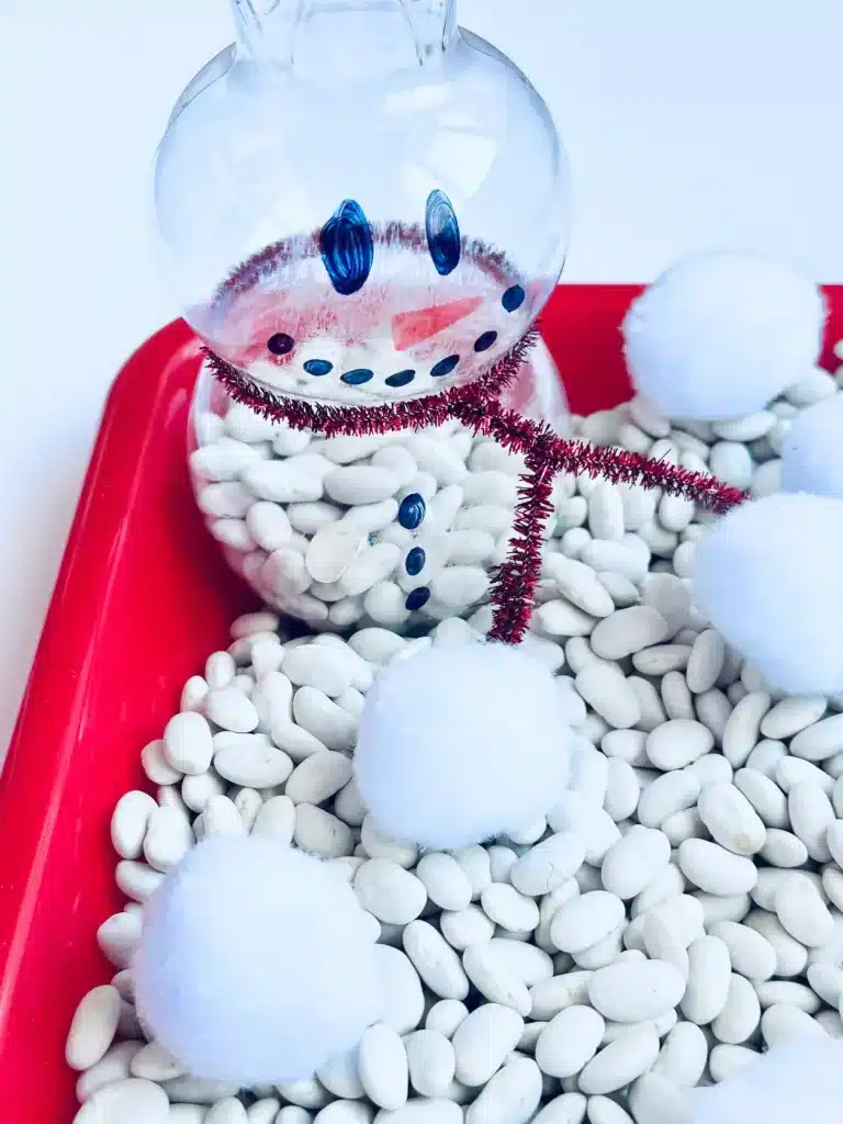 Snowman Sensory Bin - Cultivating Brilliant Minds a snowman sensory bin using beans and cotton balls and plastic bottles decorated to look like snowmen