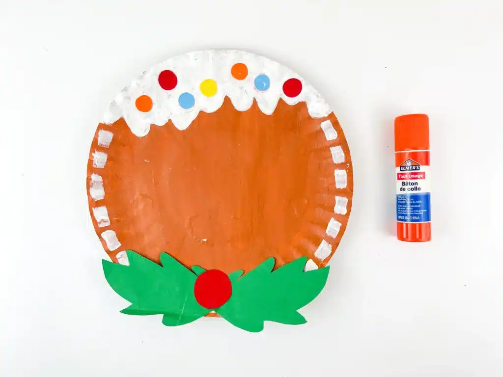 Gingerbread Paper Plate Craft - Cultivating Brilliant Minds a paper plate painted brown with white painted dots are the endge and scalloped at the top to look like icing with colored paper to look like gumdrops and a holly bow tie