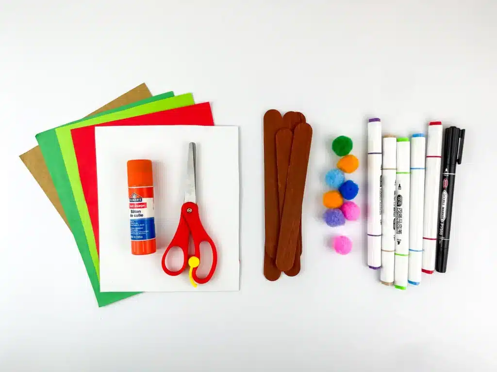 Gingerbread House Craft - Cultivating Brilliant Minds supplies for the Popsicle Stick Gingerbread House: colored construction paper, glue, scissors, popsicle sticks painted brown, pom poms, and markers