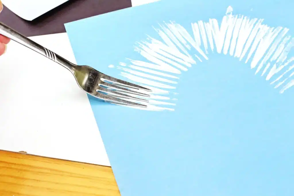 Fork Painted Abominable Snowman - Cultivating Brilliant Minds using a fork to spread white paint on a blue piece of paper