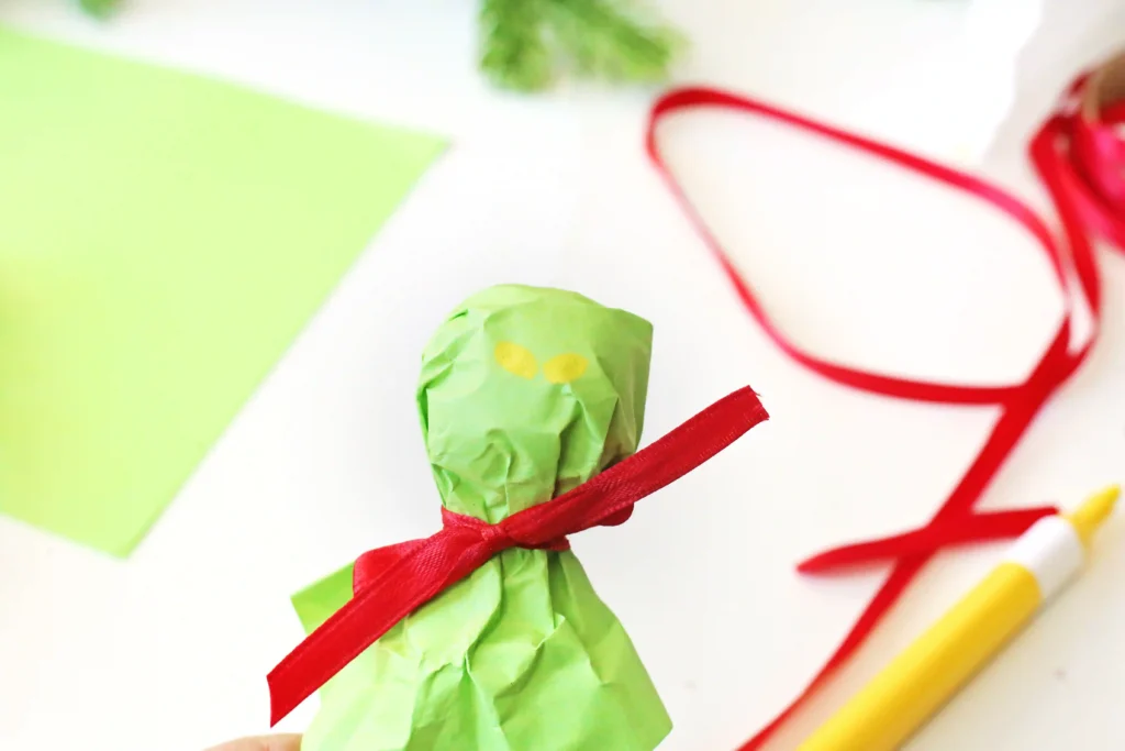 Grinch Lollipops - Cultivating Brilliant Minds a lollipop wrapped with green tissue paper and tied with a ribbon and yellow eyes drawn on