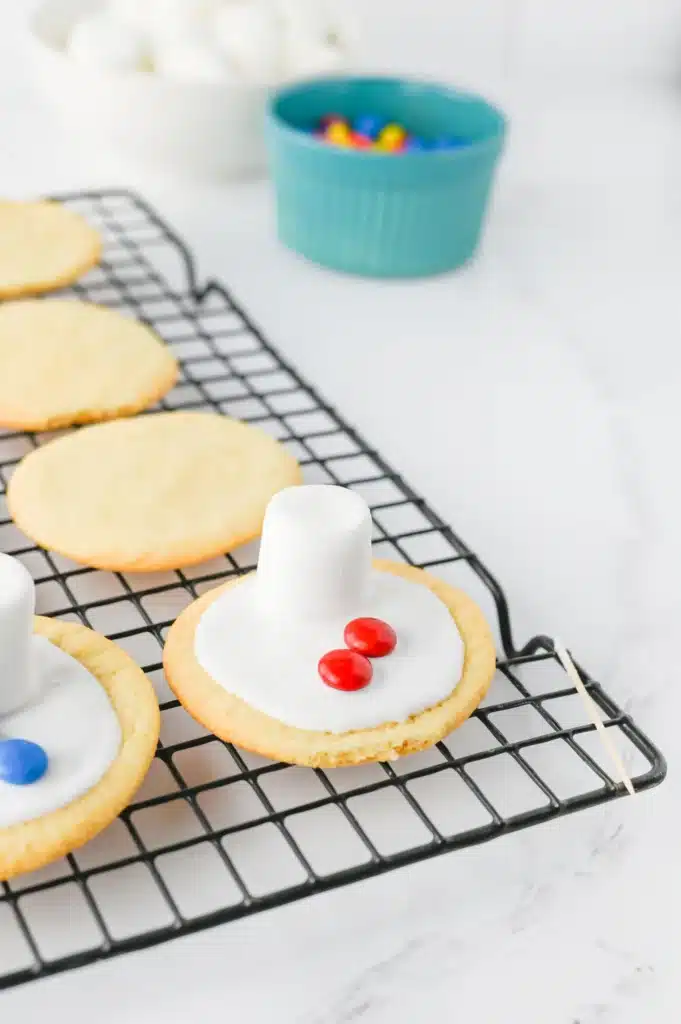 Melted Snowman Cookies - Cultivating Brilliant Minds a sugar cookie with icing and a marshmallow on top to look like a melted snowman & m&ms for buttons