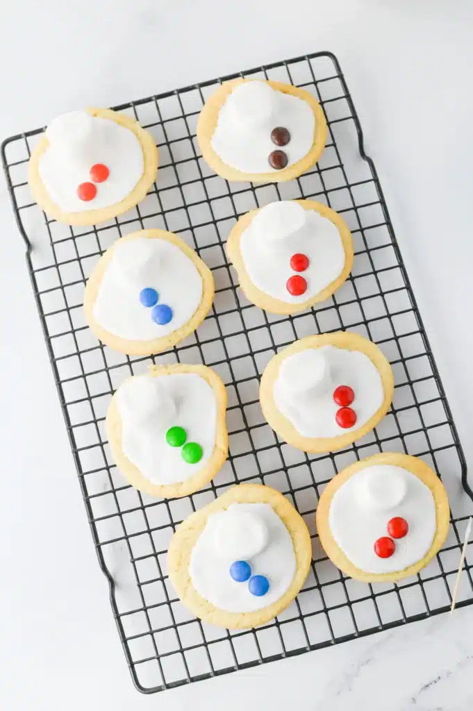 Melted Snowman Cookies - Cultivating Brilliant Minds a sugar cookie with icing and a marshmallow on top to look like a melted snowman & m&ms for buttons
