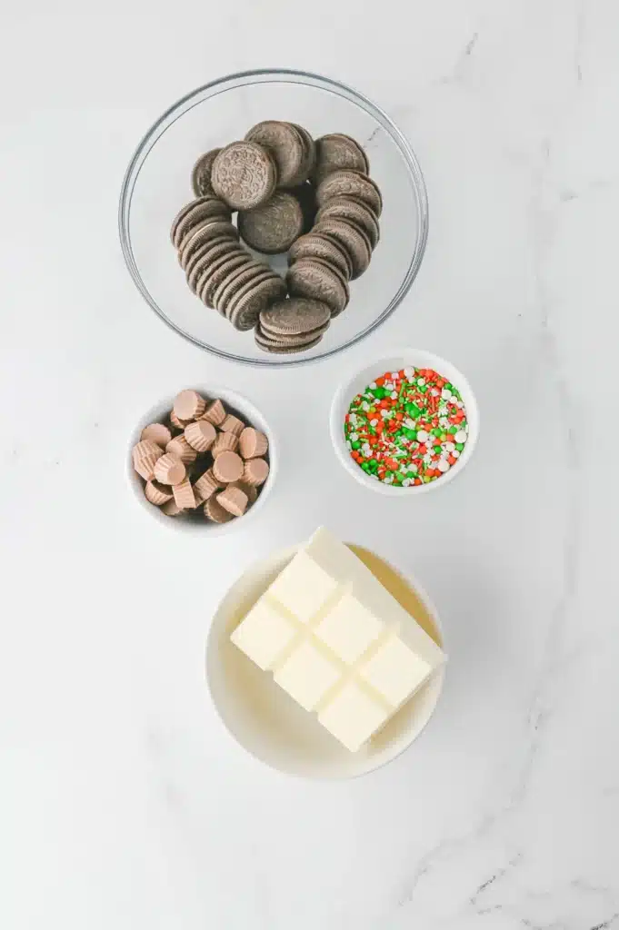 Oreo Ornament Cookies - Cultivating Brilliant Minds ingredients to make the oreo ornament cookies: oreos, vanilla chocolate bark, reeses mini cups, and christmas sprinkles