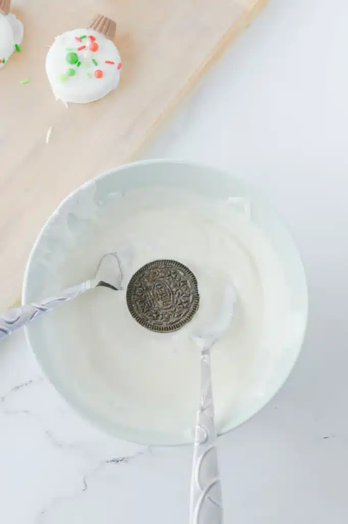 Oreo Ornament Cookies - Cultivating Brilliant Minds dipping oreos in melted vanilla almond bark
