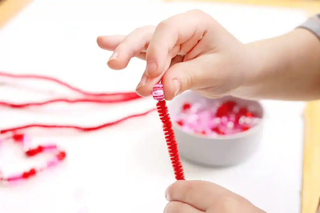 Pipe Cleaner Heart Lacing Fine Motor Activity - Cultivating Brilliant Minds a kid lacing beads onto pipe cleaners