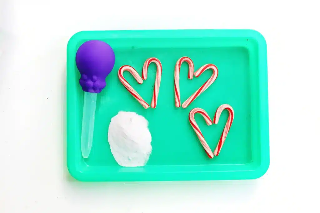 Fizzy Candy Cane Experiment - Cultivating Brilliant Minds pipette, baking soda, and candy canes on a green tray