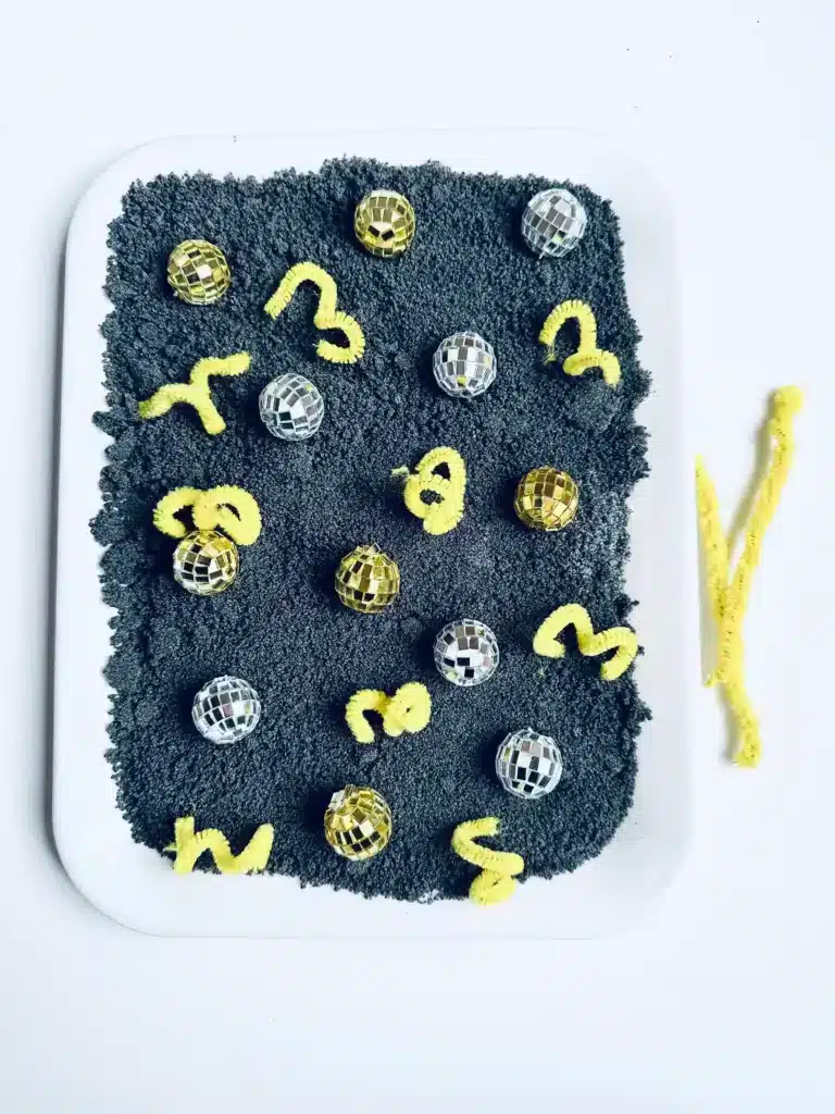 New Year's Eve Sensory Bin - Cultivating Brilliant Minds a new year's eve sensory bin with black salt, disco balls ,and yellow pipe cleaners