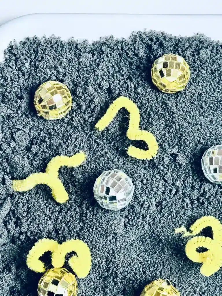 New Year's Eve Sensory Bin - Cultivating Brilliant Minds a new year's eve sensory bin with black salt, disco balls ,and yellow pipe cleaners