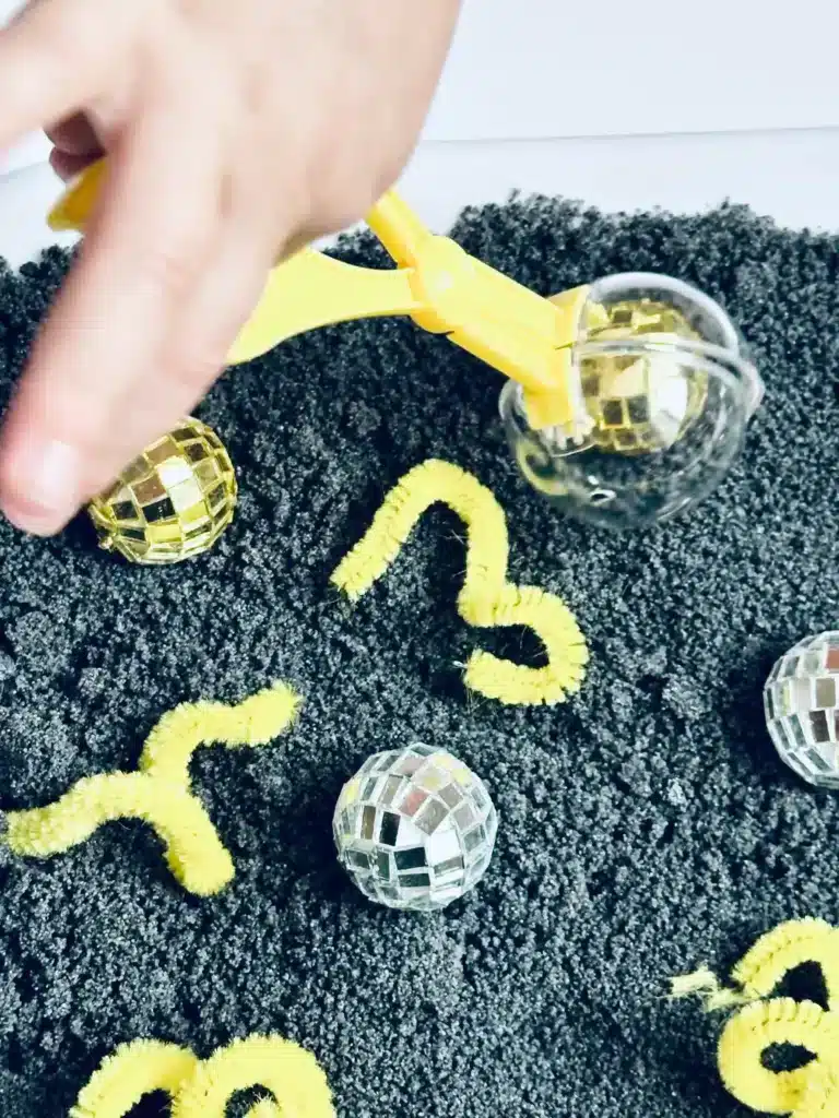 New Year's Eve Sensory Bin - Cultivating Brilliant Minds a new year's eve sensory bin with black salt, disco balls ,and yellow pipe cleaners