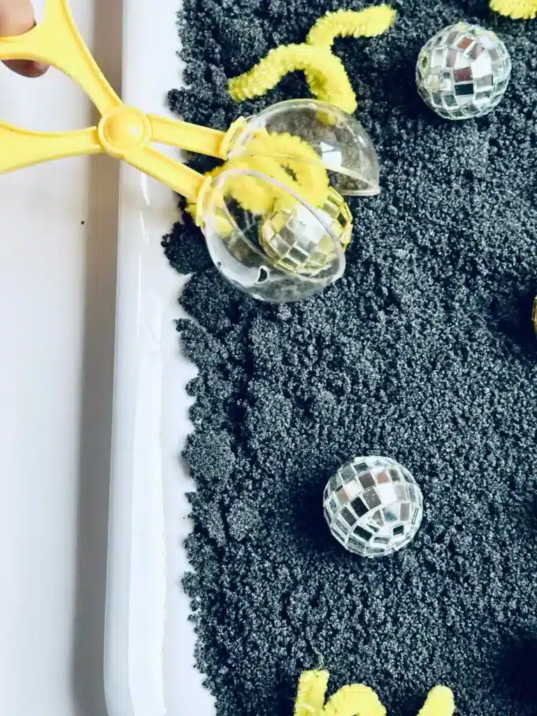 New Year's Eve Sensory Bin - Cultivating Brilliant Minds a new year's eve sensory bin with black salt, disco balls ,and yellow pipe cleaners