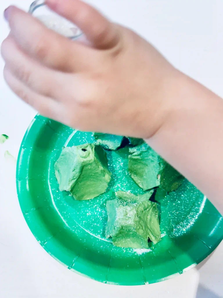 Egg Carton Sensory Bin - Cultivating Brilliant Minds adding glitter onto the green painted egg cartons