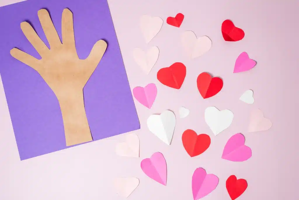 Valentine's Day Heart Tree Craft - Cultivating Brilliant Minds hearts cut out of pink, red and white construction paper next to a handprint glued onto purple paper
